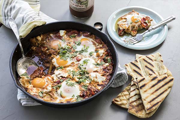 Shakshuka meal in a skillet with a plate of shakshuka nearby and some bread